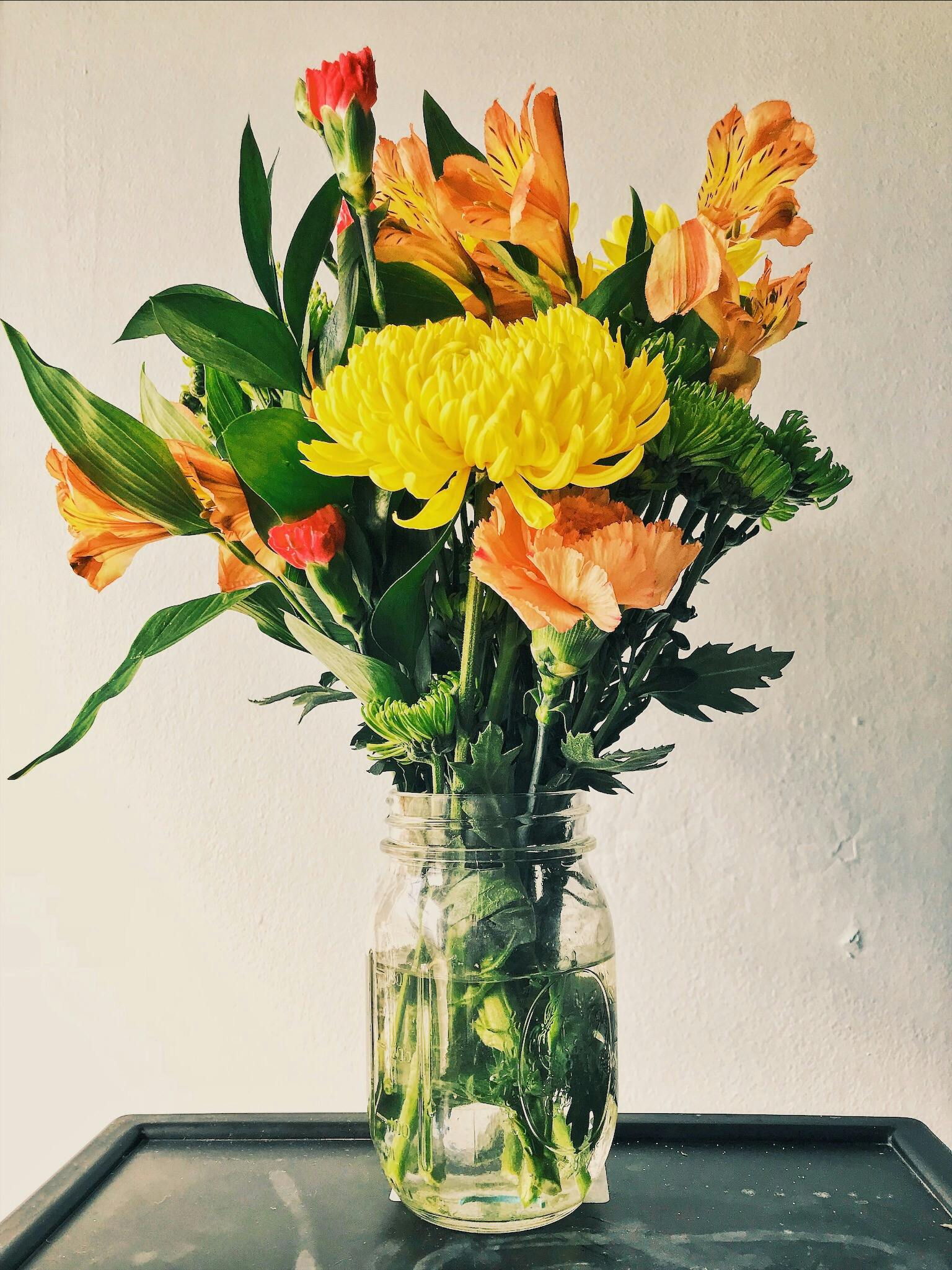 Colorful bouquet of fresh flowers in a mason jar against a simple backdrop.