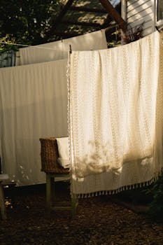 Sunlit outdoor laundry area with hanging blankets and wicker chair.